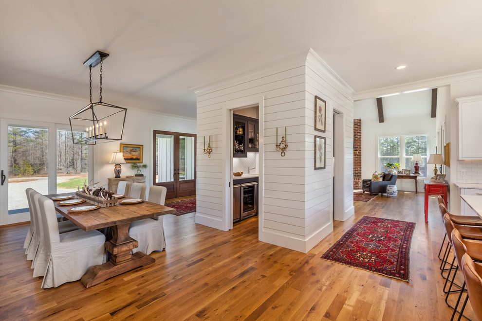 Large farmhouse kitchen/dining room in Other with white walls, medium hardwood flooring, brown floors and feature lighting.