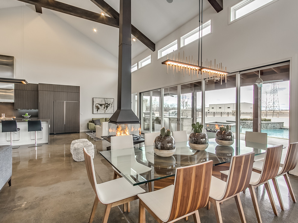 Cette image montre une salle à manger ouverte sur le salon design avec un mur gris, sol en béton ciré et cheminée suspendue.