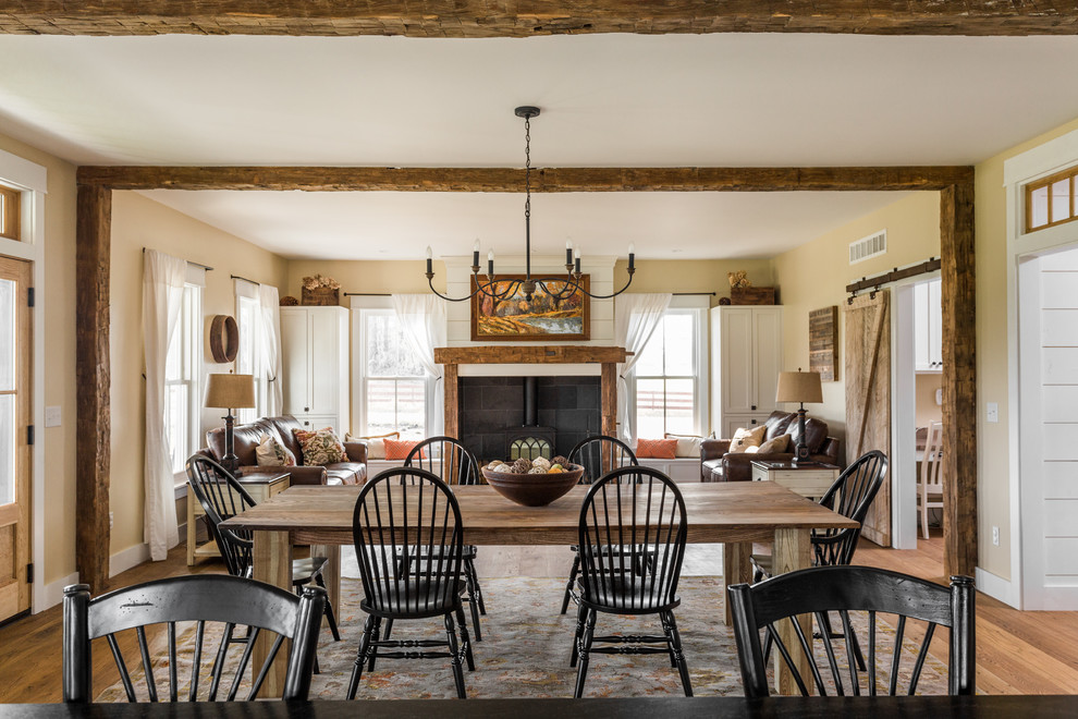 Inspiration pour une grande salle à manger ouverte sur la cuisine rustique avec un mur beige, un sol en bois brun, un poêle à bois, un manteau de cheminée en carrelage et éclairage.