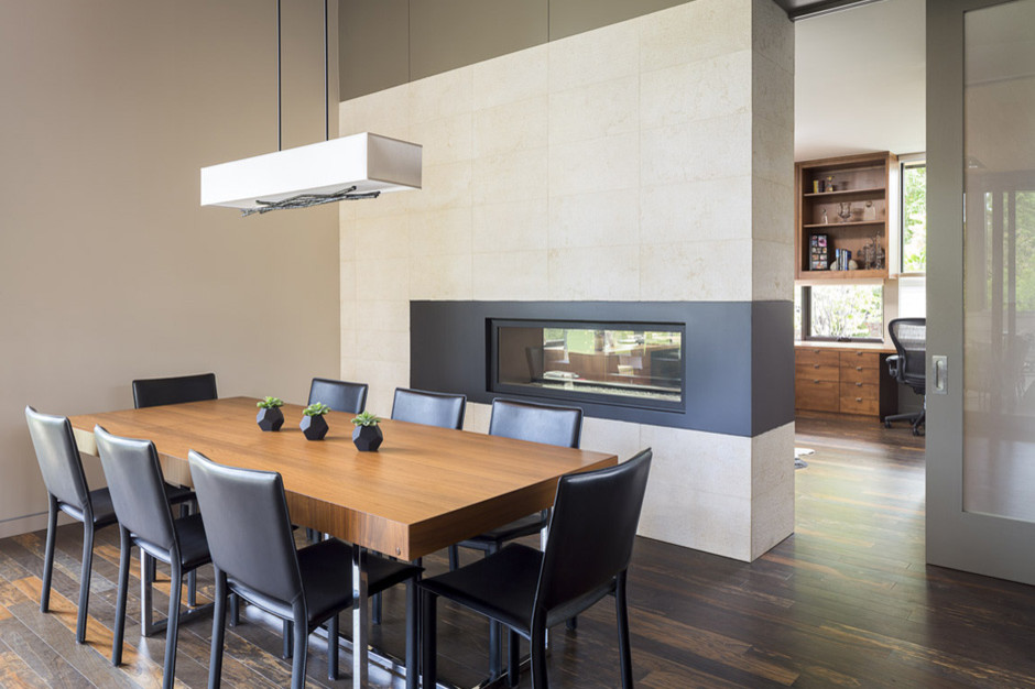 На фото: кухня-столовая среднего размера в стиле модернизм с белыми стенами, темным паркетным полом, двусторонним камином, фасадом камина из металла и коричневым полом с
