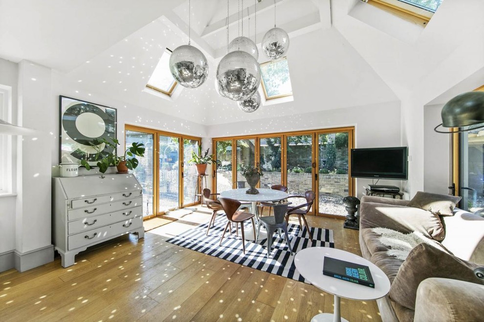 This is an example of a large contemporary open plan dining room in London with white walls, light hardwood flooring and beige floors.