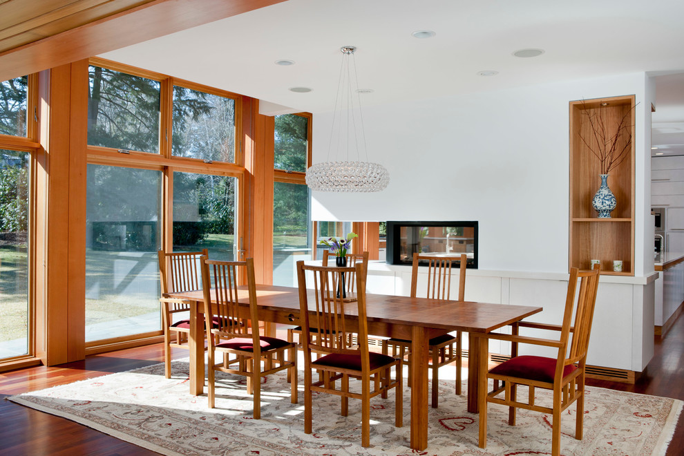 Réalisation d'une salle à manger design avec un mur blanc, un sol en bois brun et une cheminée double-face.