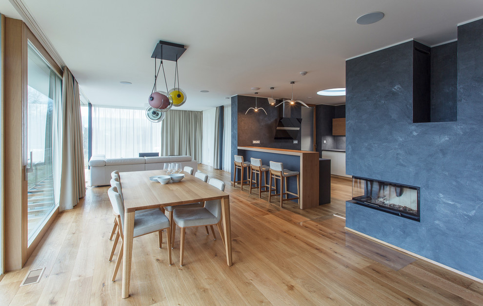 Große Moderne Wohnküche mit weißer Wandfarbe, braunem Holzboden, Kaminumrandung aus Holz und Tunnelkamin in Sonstige