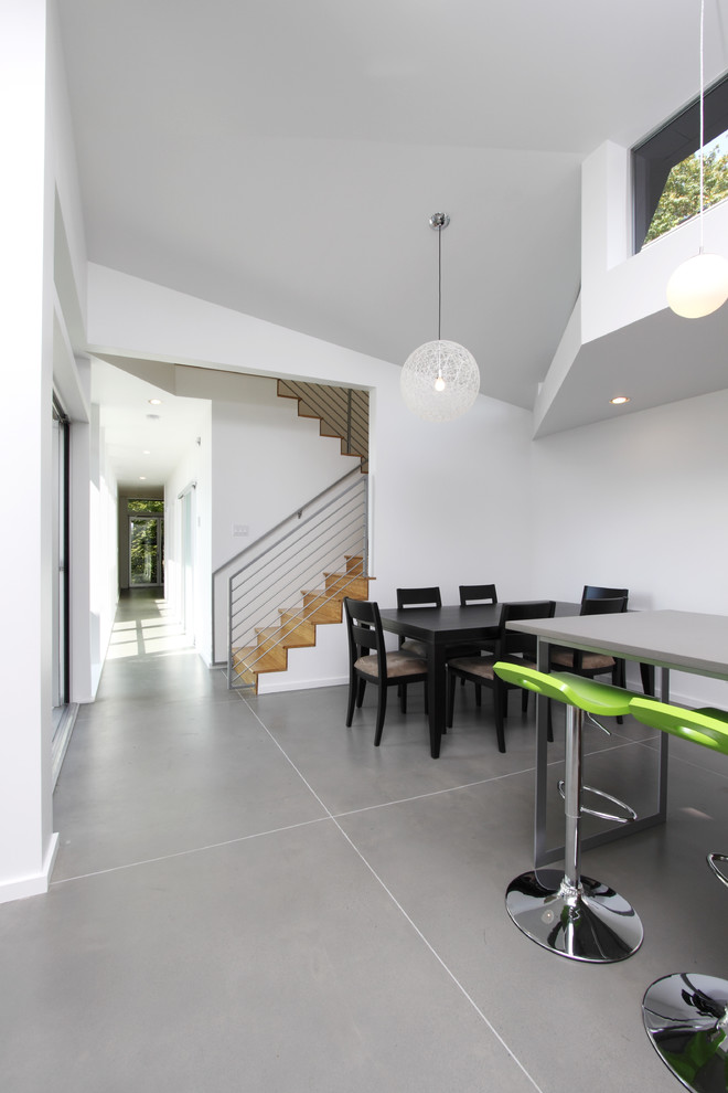 Immagine di una sala da pranzo aperta verso la cucina minimalista con pareti bianche, pavimento in cemento e pavimento grigio