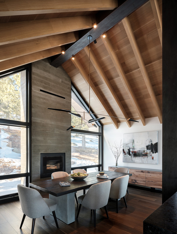 Idée de décoration pour une salle à manger ouverte sur la cuisine chalet de taille moyenne avec un mur blanc, un sol en bois brun, une cheminée standard et un manteau de cheminée en béton.