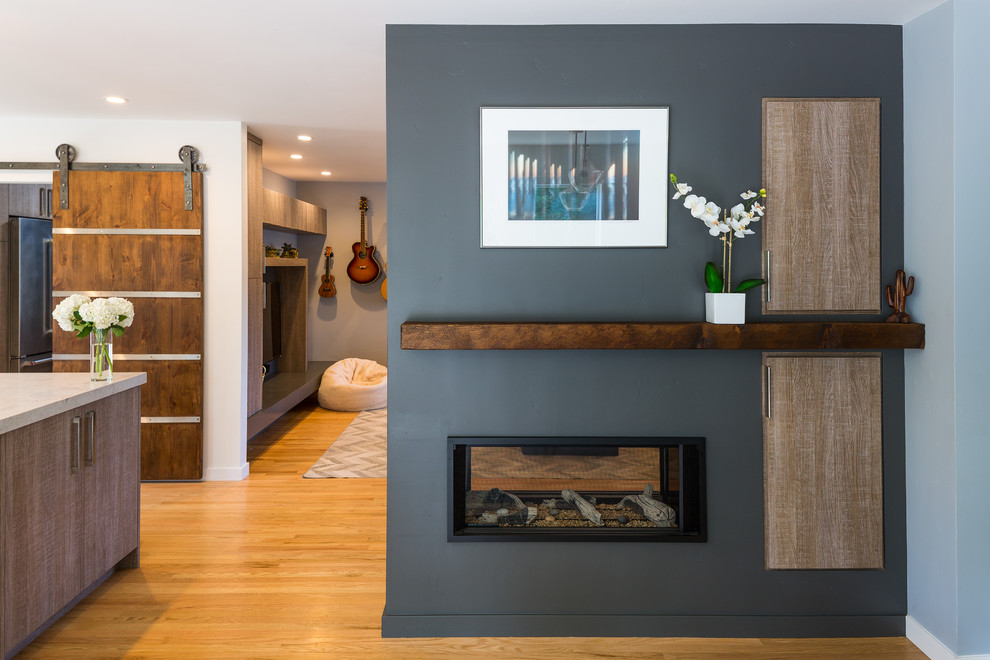 Mittelgroße Moderne Wohnküche mit grauer Wandfarbe, hellem Holzboden, Tunnelkamin, verputzter Kaminumrandung und braunem Boden in Sonstige