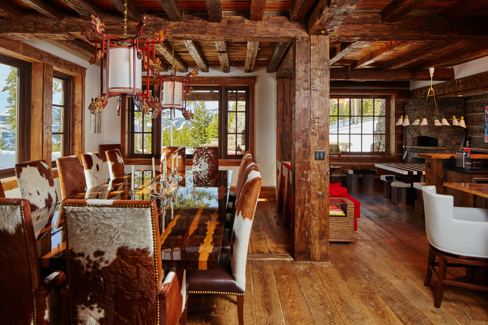 Idée de décoration pour une salle à manger ouverte sur la cuisine chalet avec un mur blanc, un sol en bois brun et un poêle à bois.