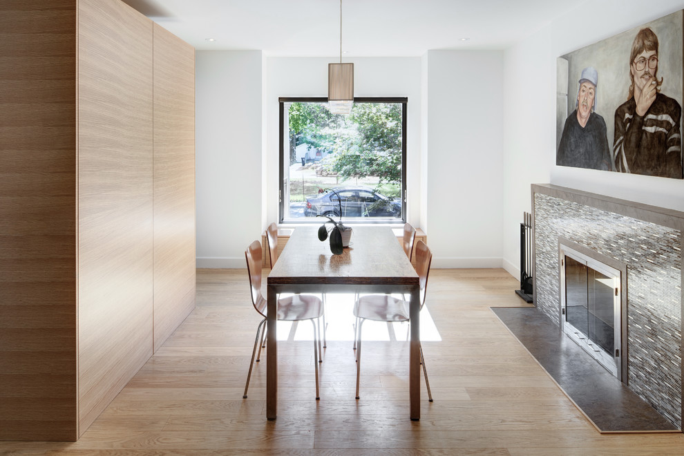 This is an example of a medium sized modern enclosed dining room in Toronto with white walls, light hardwood flooring, a standard fireplace and a tiled fireplace surround.