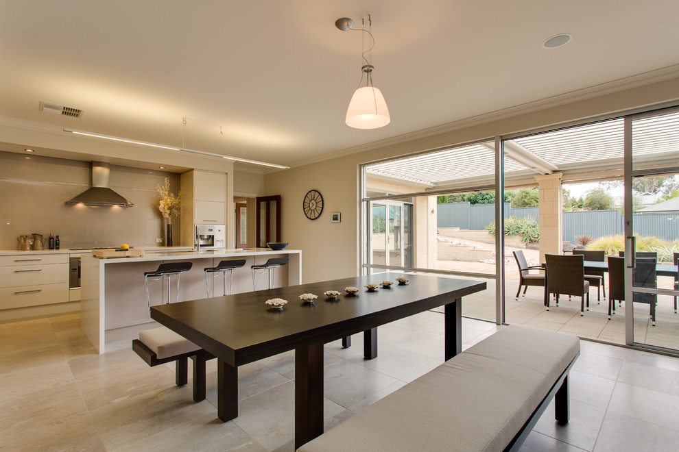 Immagine di una grande sala da pranzo aperta verso la cucina minimalista con pareti beige e pavimento in travertino