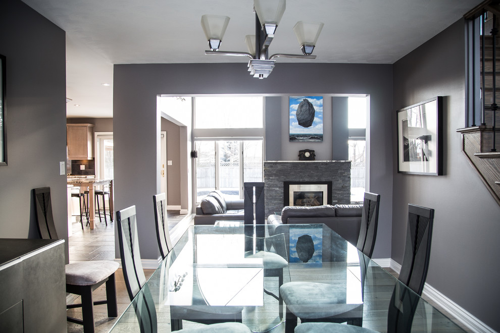 Exemple d'une grande salle à manger ouverte sur le salon tendance avec un mur gris, parquet clair, une cheminée standard et un manteau de cheminée en pierre.