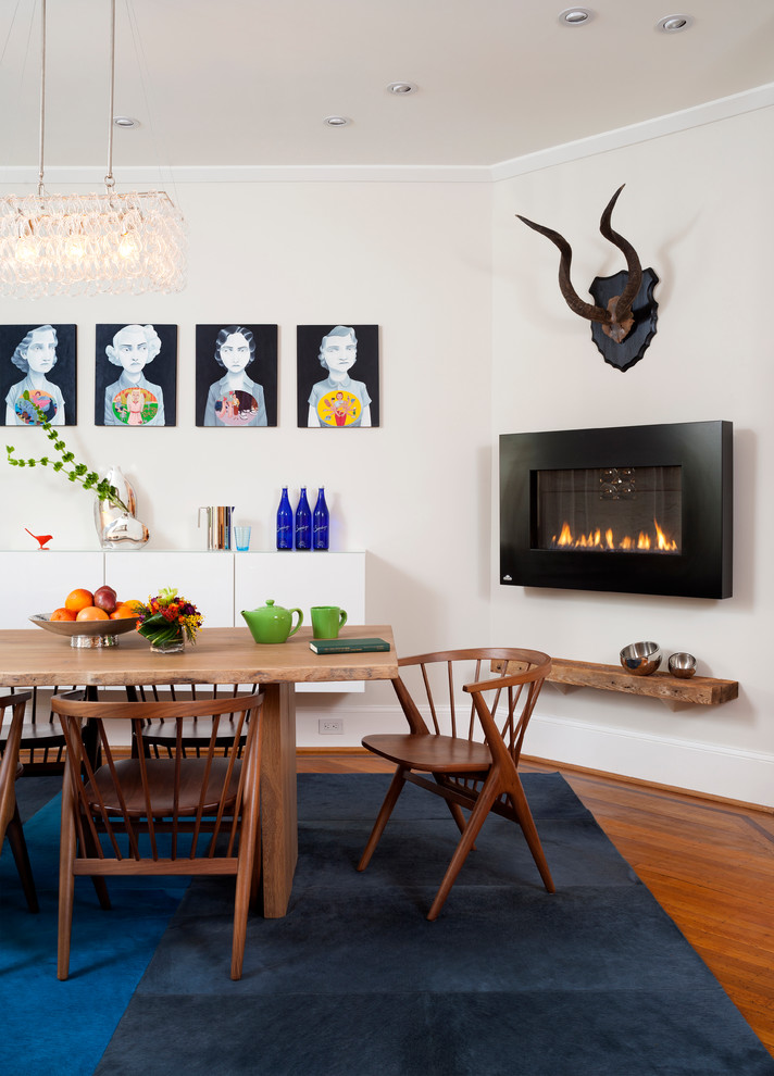 Cette image montre une grande salle à manger ouverte sur le salon vintage avec un mur blanc, un sol en bois brun, un manteau de cheminée en métal, une cheminée ribbon et un sol marron.