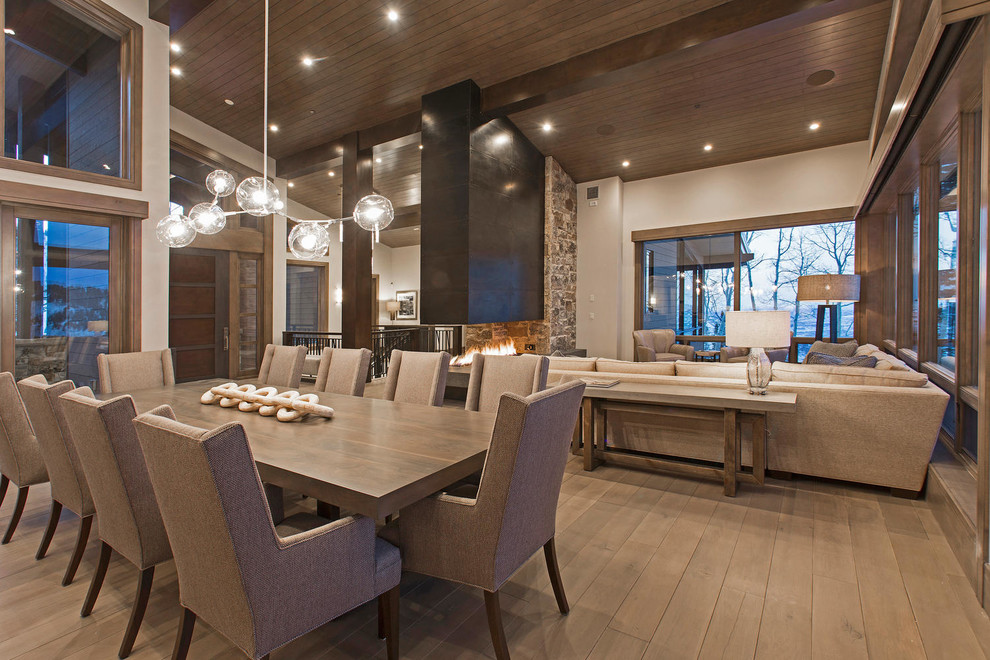 Cette photo montre une très grande salle à manger ouverte sur le salon tendance avec un mur gris, un sol en bois brun, une cheminée double-face, un manteau de cheminée en métal et un plafond en bois.