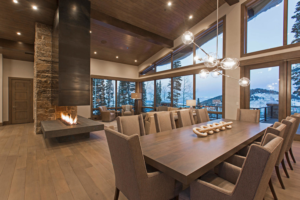 Exemple d'une très grande salle à manger ouverte sur le salon tendance avec un mur gris, un sol en bois brun, une cheminée double-face, un manteau de cheminée en métal et éclairage.