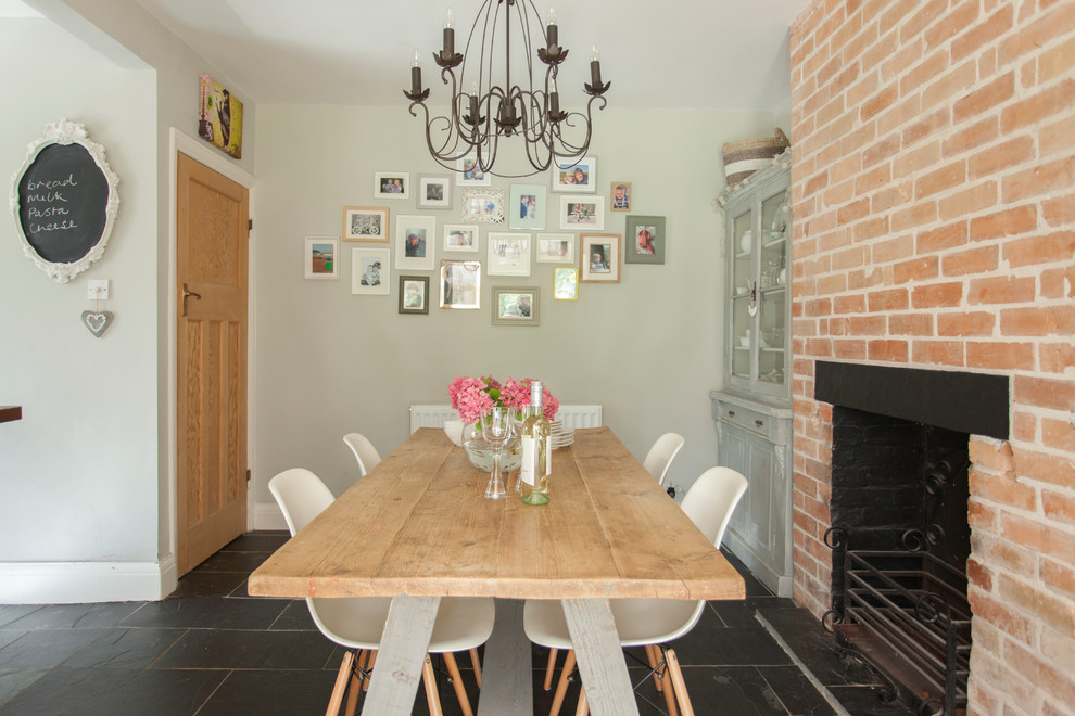 Foto di una sala da pranzo stile shabby di medie dimensioni con pareti grigie, camino classico, cornice del camino in mattoni e pavimento nero