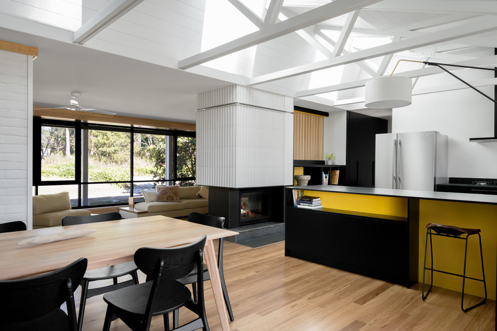 Стильный дизайн: большая кухня-столовая в стиле ретро с белыми стенами, паркетным полом среднего тона, двусторонним камином и фасадом камина из плитки - последний тренд