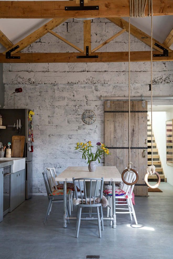 Diseño de comedor rural grande abierto sin chimenea con paredes blancas, suelo de cemento y suelo gris