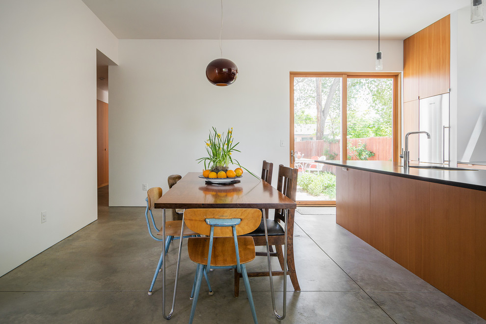 Cette photo montre une salle à manger ouverte sur la cuisine moderne avec un mur blanc et sol en béton ciré.