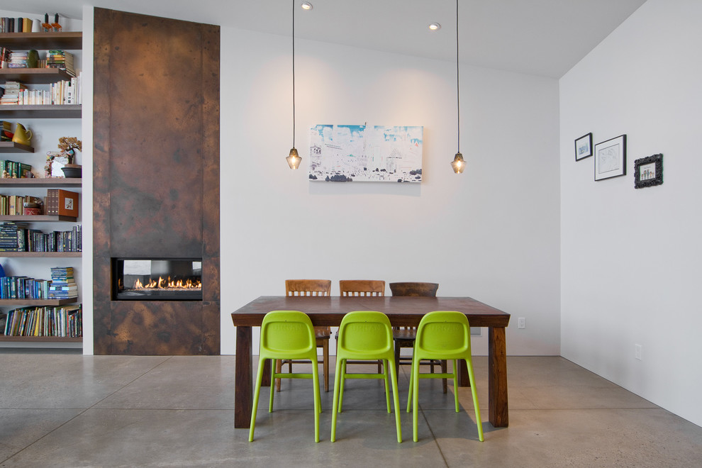 Cette image montre une salle à manger design avec sol en béton ciré, un manteau de cheminée en métal et une cheminée ribbon.