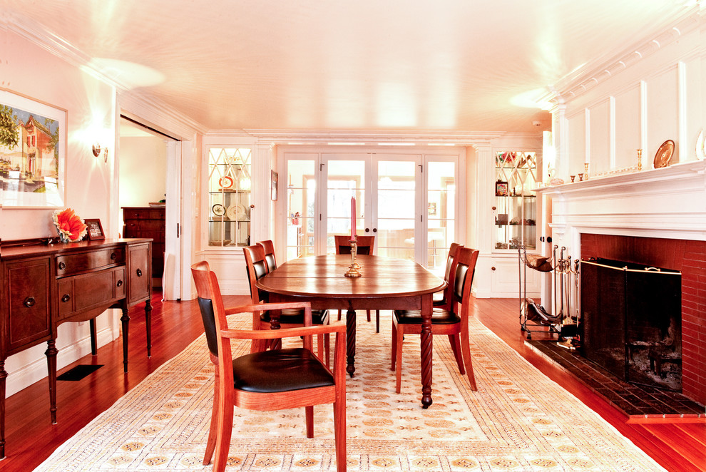 Cette image montre une salle à manger traditionnelle avec un mur blanc, parquet foncé et un manteau de cheminée en brique.