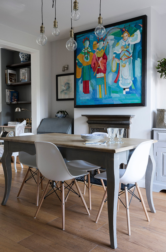 Example of a transitional light wood floor dining room design in London with white walls and a standard fireplace