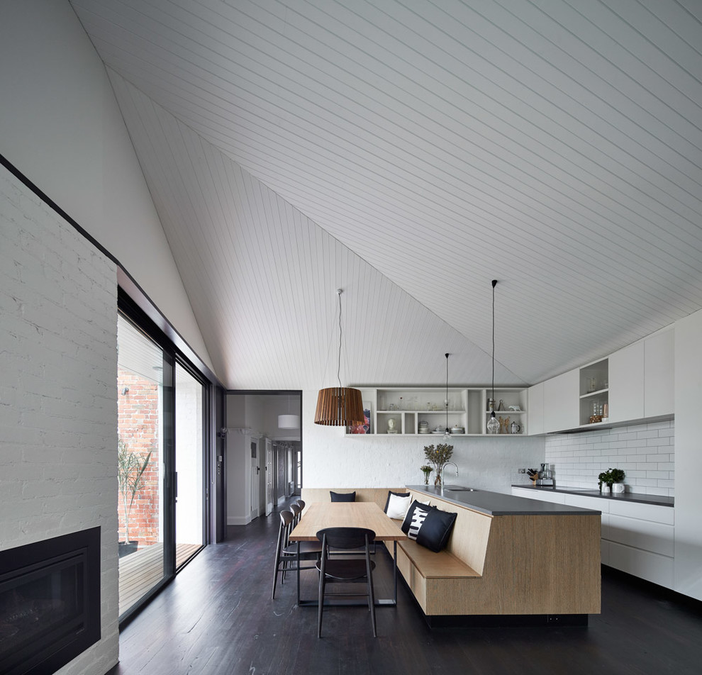 Свежая идея для дизайна: кухня-столовая в стиле модернизм с белыми стенами, темным паркетным полом, стандартным камином и фасадом камина из кирпича - отличное фото интерьера