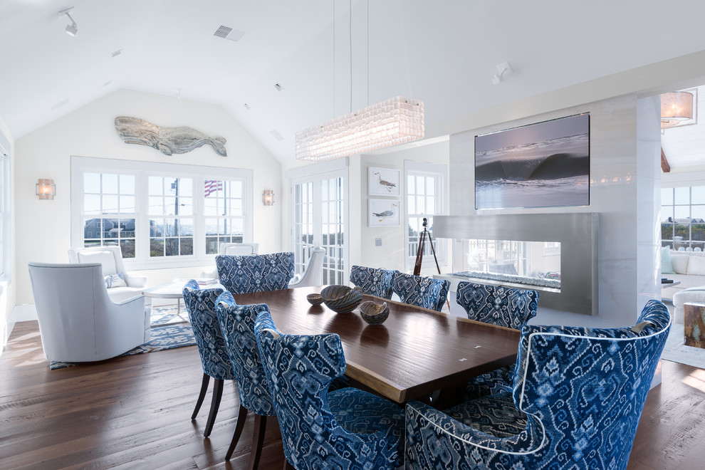 Inspiration for a beach style open plan dining room in Boston with white walls, dark hardwood flooring, a two-sided fireplace, a metal fireplace surround and feature lighting.