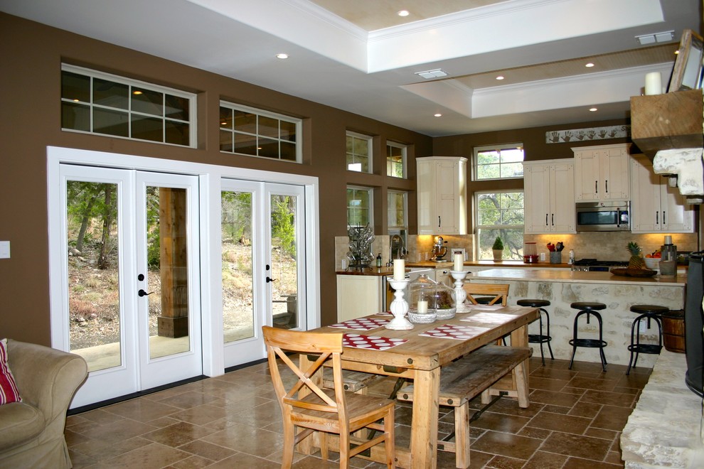 Idée de décoration pour une salle à manger ouverte sur la cuisine champêtre de taille moyenne avec un mur marron, un sol en travertin, une cheminée standard, un manteau de cheminée en pierre et un sol marron.