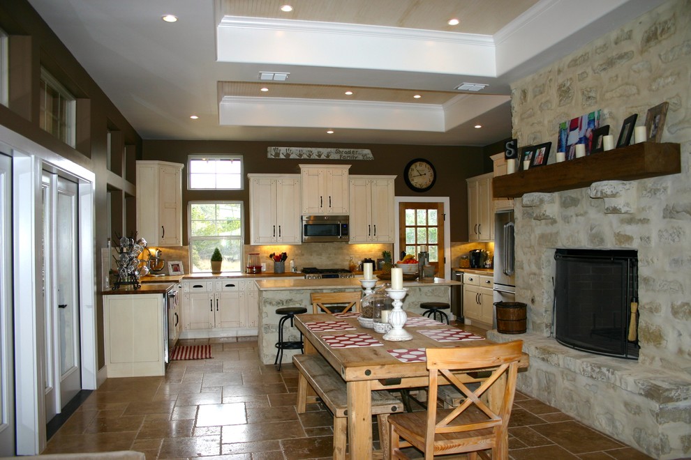 オースティンにある中くらいなカントリー風のおしゃれなダイニングキッチン (茶色い壁、トラバーチンの床、茶色い床、標準型暖炉、石材の暖炉まわり) の写真