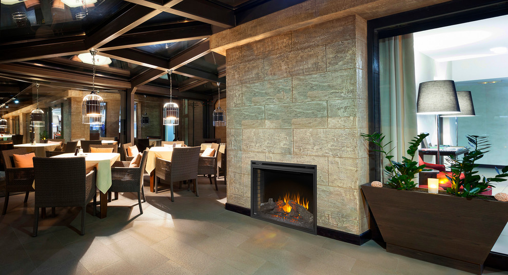 На фото: большая гостиная-столовая в стиле рустика с коричневыми стенами, полом из керамогранита, стандартным камином, фасадом камина из камня и бежевым полом с