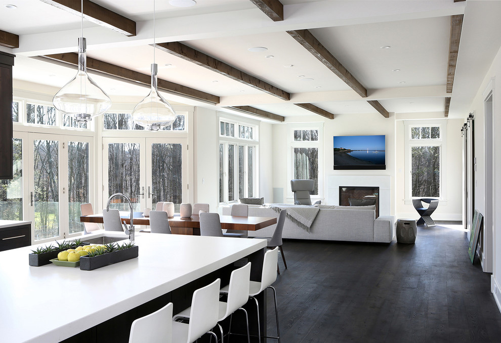 Immagine di un'ampia sala da pranzo aperta verso la cucina contemporanea con pareti bianche, parquet scuro, camino classico e cornice del camino in cemento
