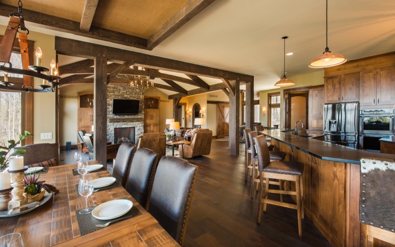 This is an example of an expansive rustic kitchen/dining room in New York with dark hardwood flooring, a stone fireplace surround, brown floors, brown walls and no fireplace.