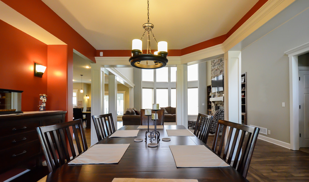Cette image montre une grande salle à manger ouverte sur le salon craftsman avec un mur orange, parquet foncé, une cheminée standard et un manteau de cheminée en pierre.