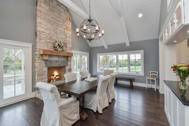Cette photo montre une grande salle à manger ouverte sur la cuisine craftsman avec un mur gris, parquet foncé, une cheminée standard et un manteau de cheminée en pierre.