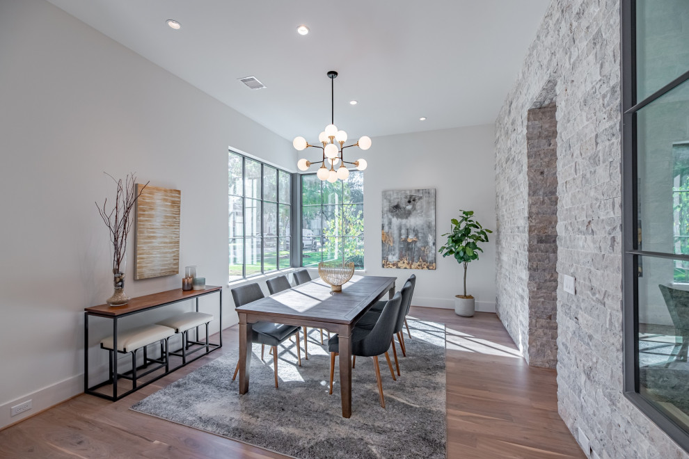 Large contemporary enclosed dining room in Houston with white walls, light hardwood flooring and brick walls.
