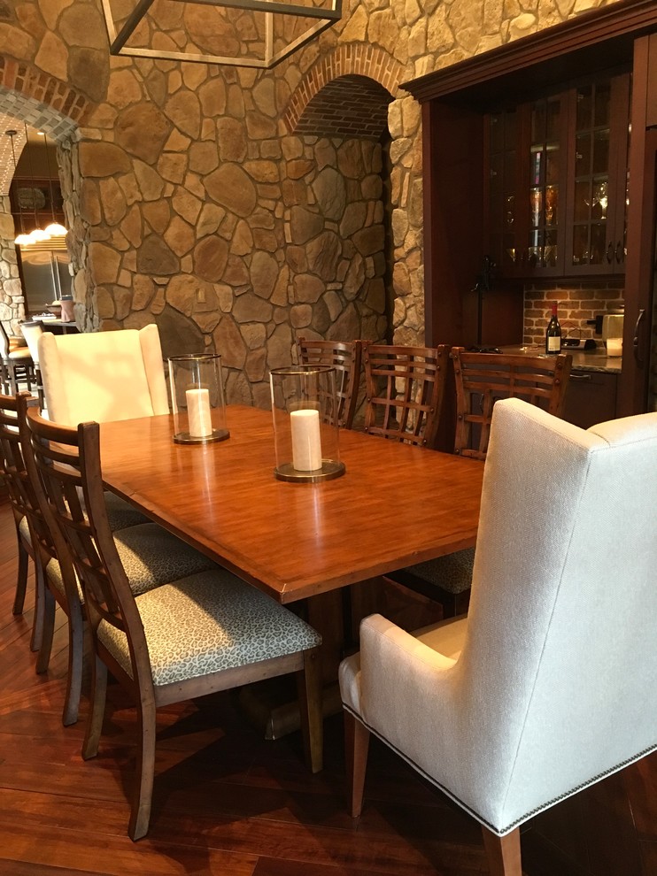 Aménagement d'une grande salle à manger ouverte sur la cuisine méditerranéenne avec un sol en bois brun, une cheminée double-face, un manteau de cheminée en pierre et un mur gris.