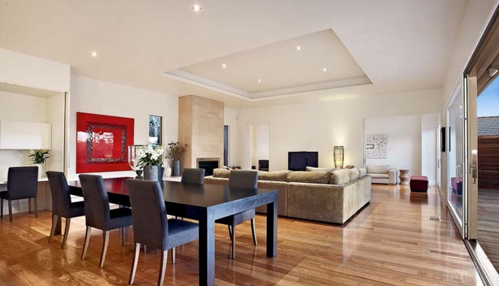 Offenes, Großes Modernes Esszimmer mit beiger Wandfarbe, braunem Holzboden, Kamin und Kaminumrandung aus Stein in Melbourne