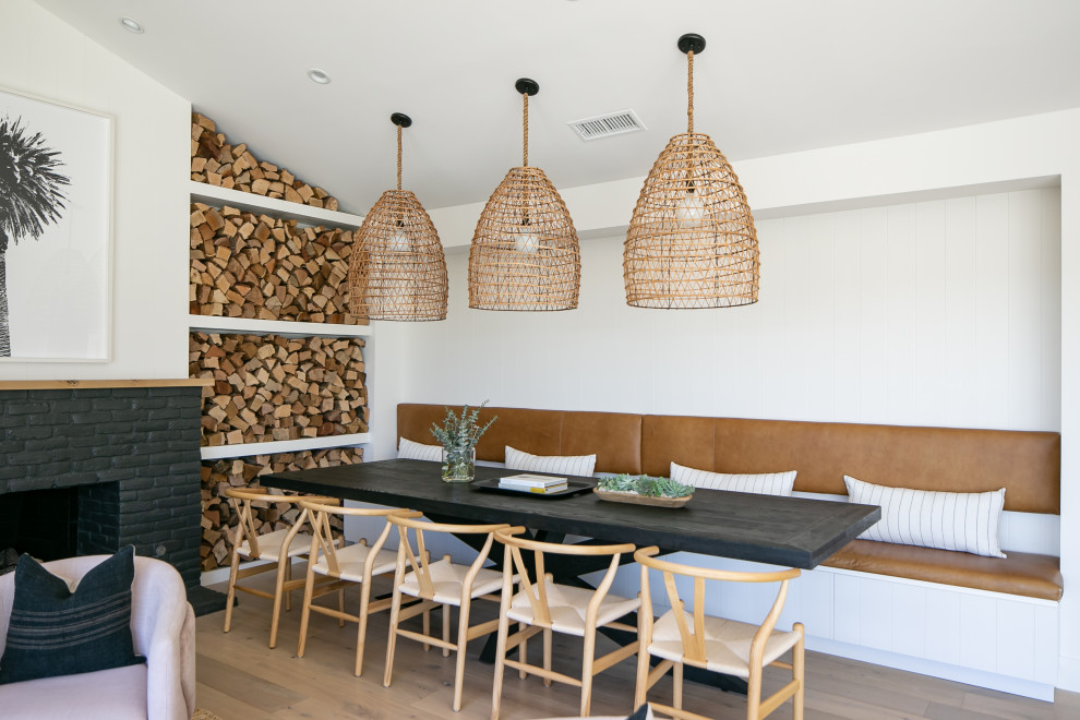 Idées déco pour une salle à manger ouverte sur le salon bord de mer avec un mur blanc, un sol en bois brun, une cheminée standard, un manteau de cheminée en brique et un sol marron.