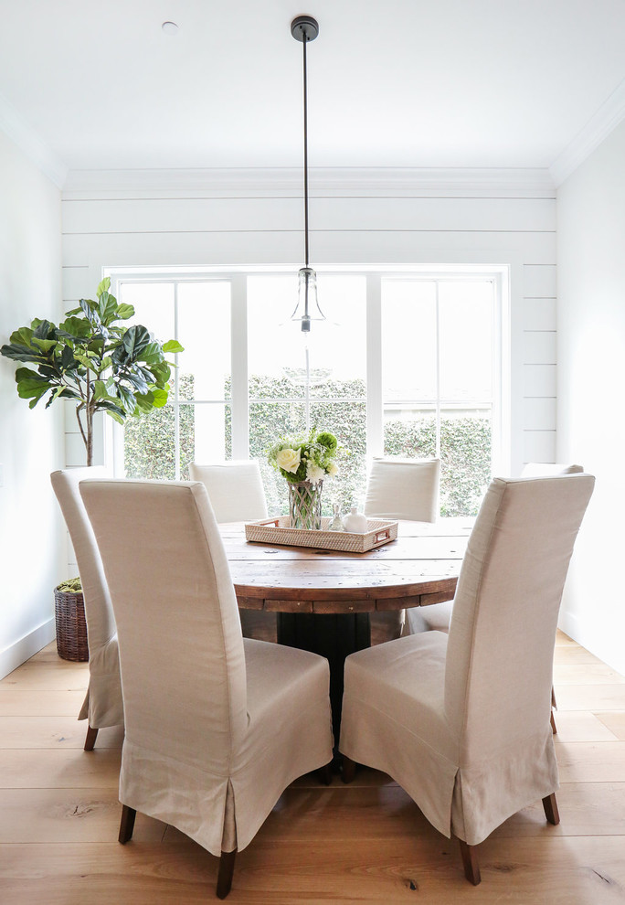 Cette image montre une salle à manger ouverte sur la cuisine rustique avec un mur blanc et parquet clair.