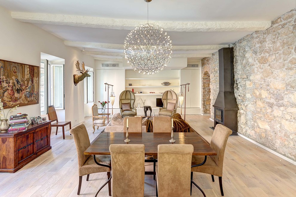 Immagine di una sala da pranzo aperta verso il soggiorno country con pareti bianche, parquet chiaro e stufa a legna