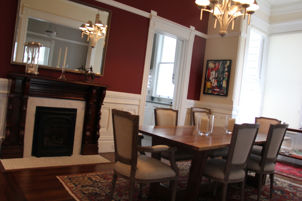 Aménagement d'une salle à manger classique fermée avec un mur rouge, un sol en bois brun et un manteau de cheminée en pierre.