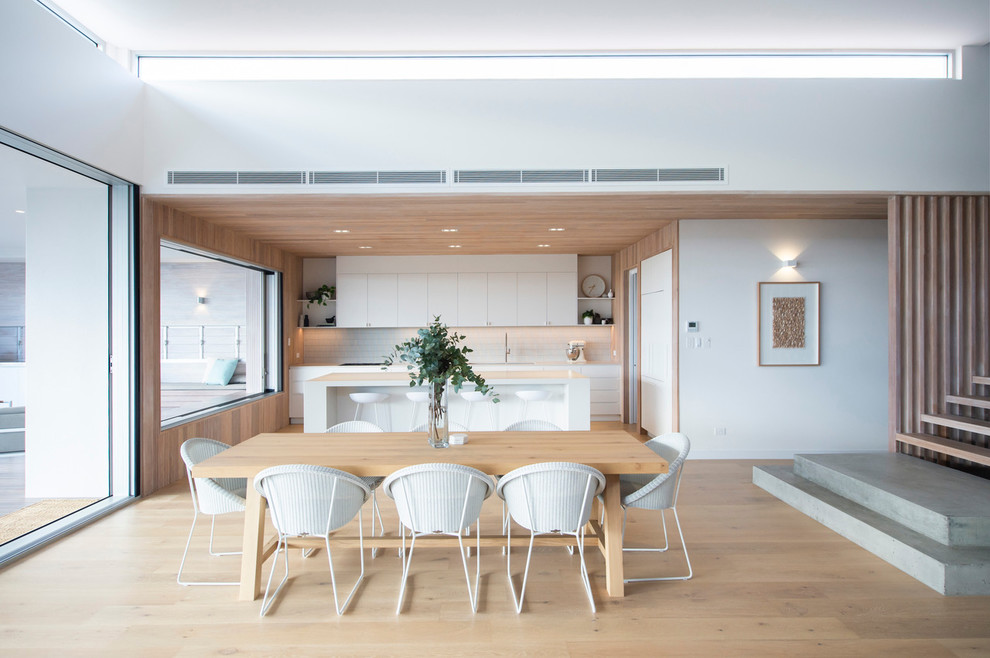Foto di una sala da pranzo aperta verso la cucina contemporanea con pareti bianche, parquet chiaro e pavimento beige