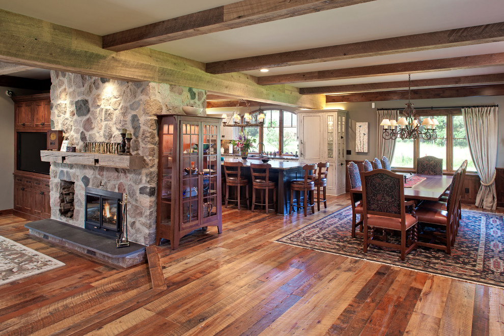 Exemple d'une grande salle à manger ouverte sur la cuisine avec un sol en bois brun et un manteau de cheminée en pierre.