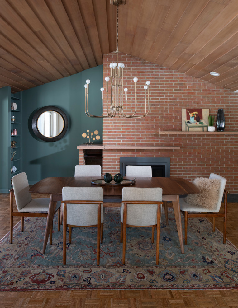 Cette photo montre une grande salle à manger ouverte sur la cuisine rétro avec un mur vert, une cheminée standard, un manteau de cheminée en brique, un sol marron et un sol en bois brun.