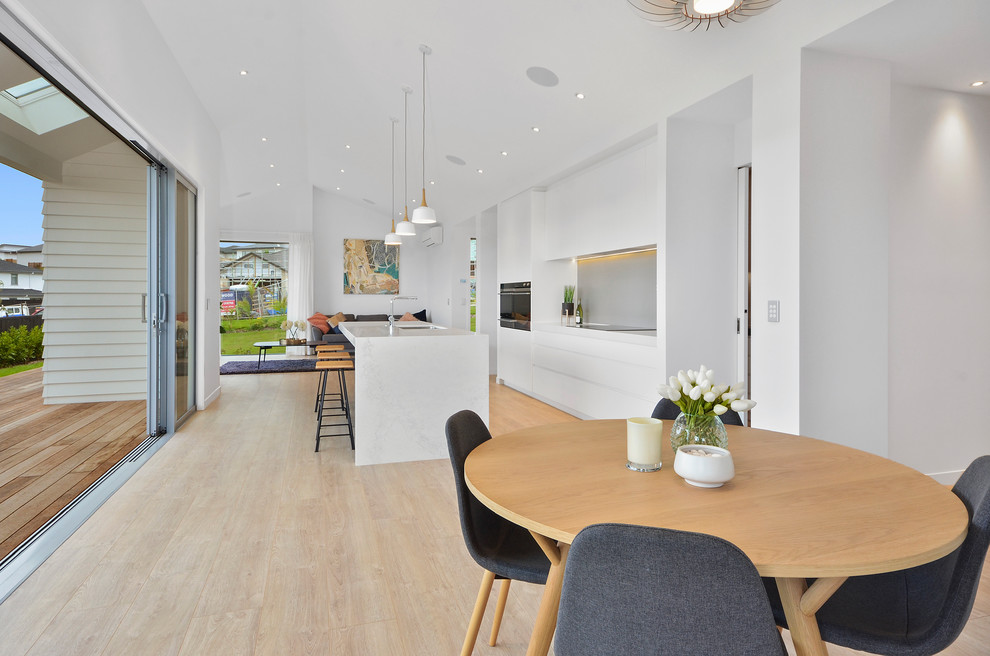 Expansive modern kitchen/dining room in Auckland with white walls, light hardwood flooring and brown floors.
