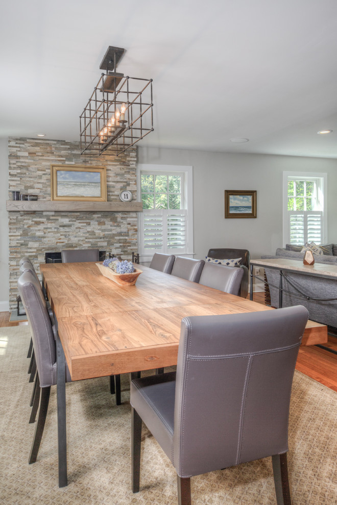 Cette photo montre une salle à manger ouverte sur le salon chic de taille moyenne avec un mur gris, un sol en bois brun, une cheminée standard, un manteau de cheminée en pierre et un sol marron.