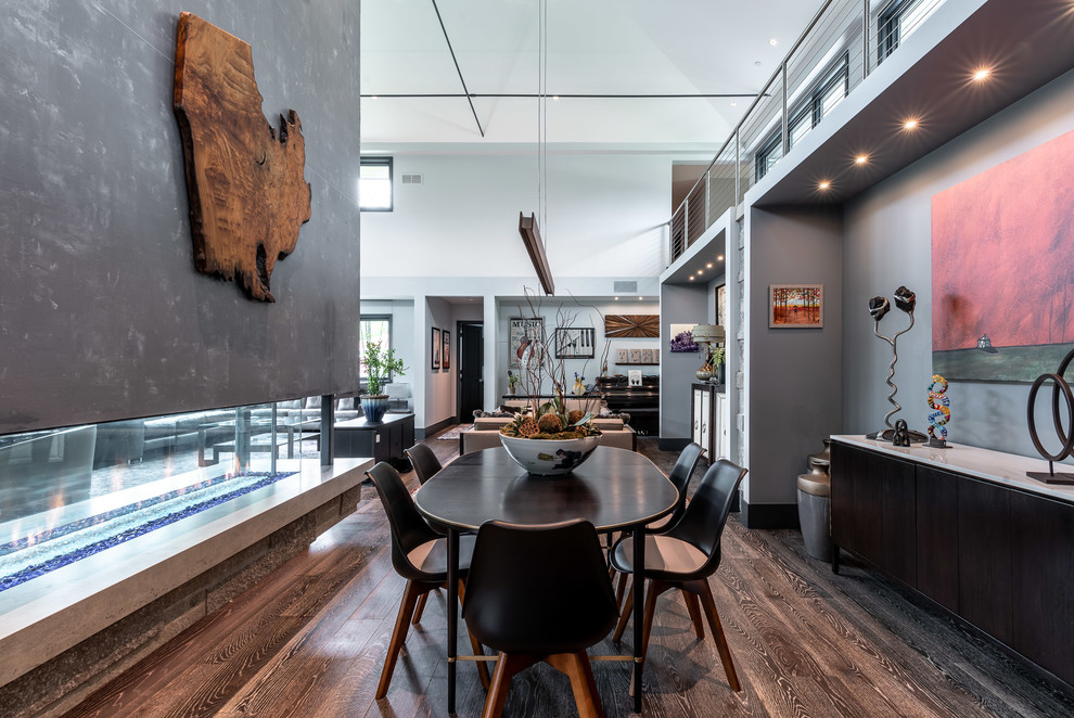 Aménagement d'une salle à manger ouverte sur le salon contemporaine avec un mur gris, parquet foncé, une cheminée double-face et un sol marron.
