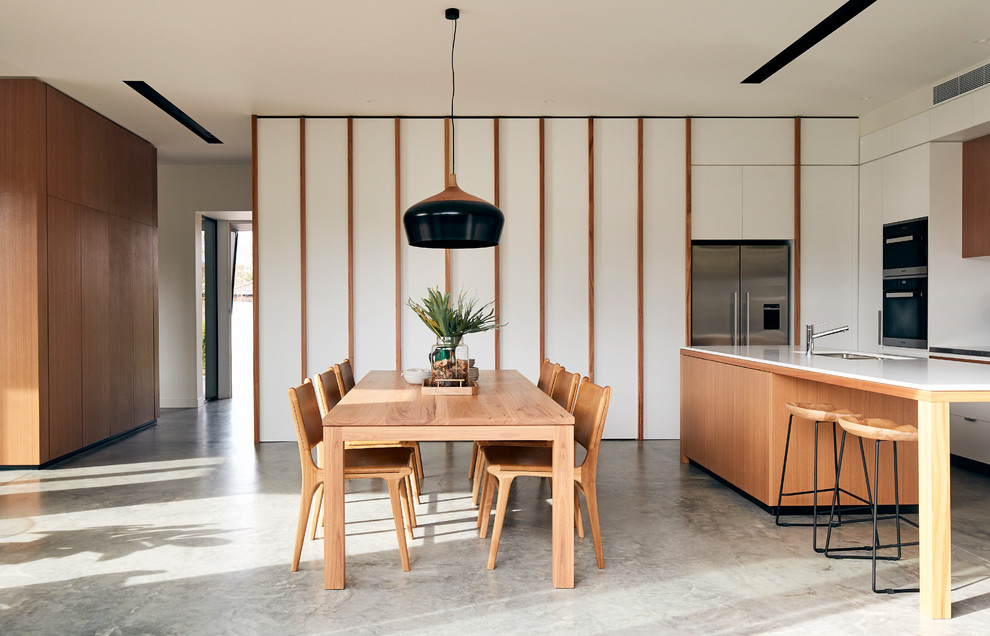 Imagen de comedor minimalista abierto con paredes blancas, suelo de cemento y suelo gris