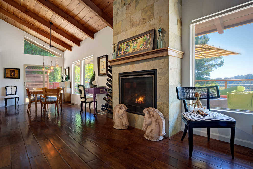 Idée de décoration pour une grande salle à manger ouverte sur le salon chalet avec un mur blanc, parquet foncé, une cheminée standard, un manteau de cheminée en pierre et un sol marron.