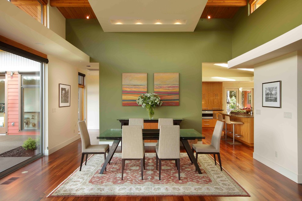 Immagine di una sala da pranzo aperta verso il soggiorno minimalista con pareti verdi e parquet scuro