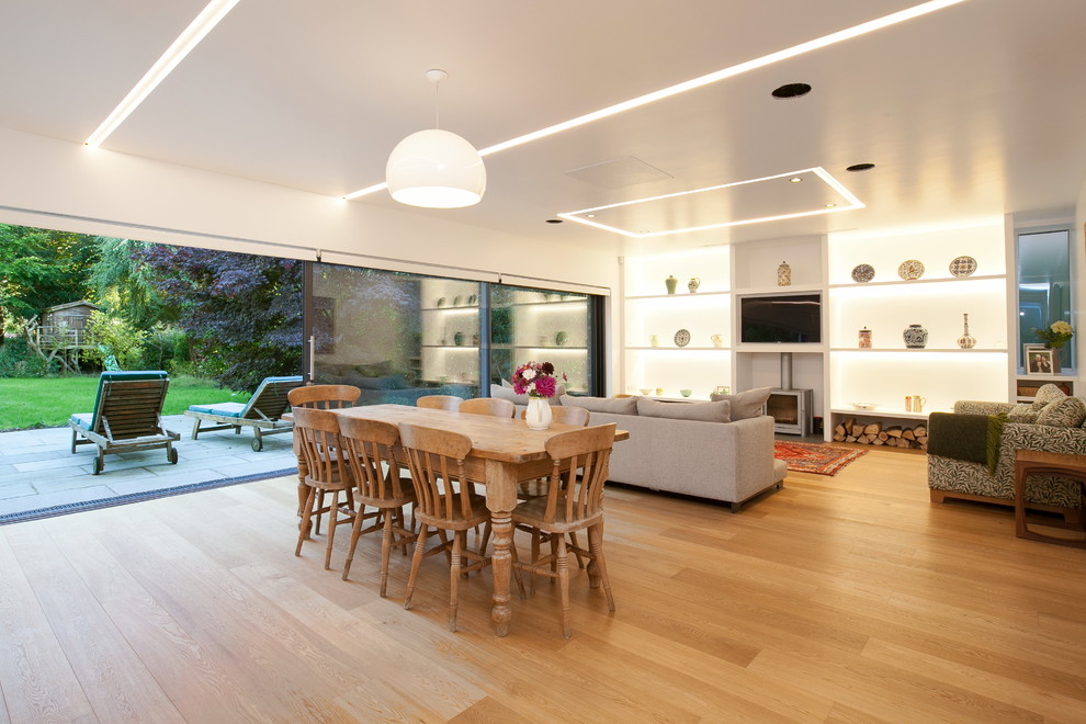 Immagine di una sala da pranzo aperta verso il soggiorno minimal con pareti bianche, pavimento in legno massello medio, stufa a legna e pavimento marrone